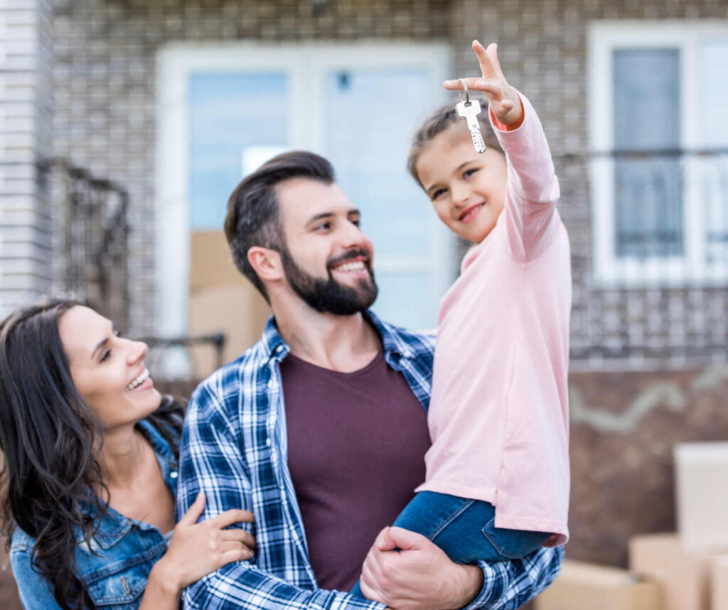 Żona i mąż z córka na rękach stoja przed swoim domem