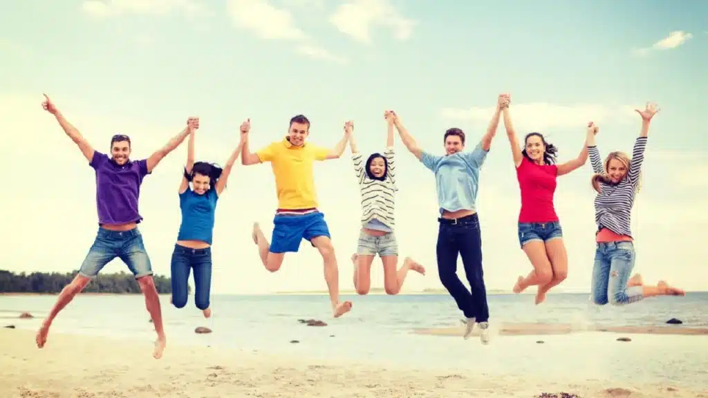 TARCZA Ubezpieczenie Turystyczne - Grupa ludzi skacze na plaży.